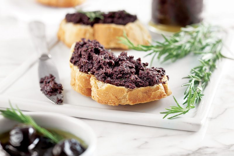 Tapenade auf Baguettebrot mit etwas Rosmarin und Oliven angerichtet