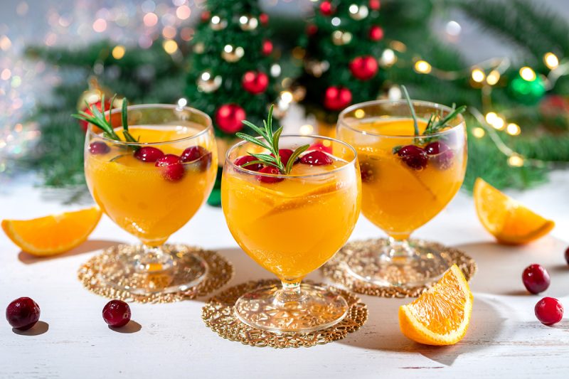 Fruchtiger Orangenpunsch im Glas mit Cranberrys und Rosmarin, weihnachtlich dekoriert